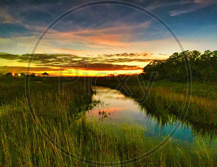 Sunset Marsh Grass Estuary With Colorful Clouds Reflecting In Creek