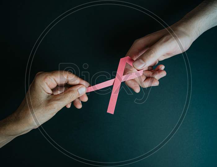 An Old Hand Giving A Pink Ribbon To A Young Hand