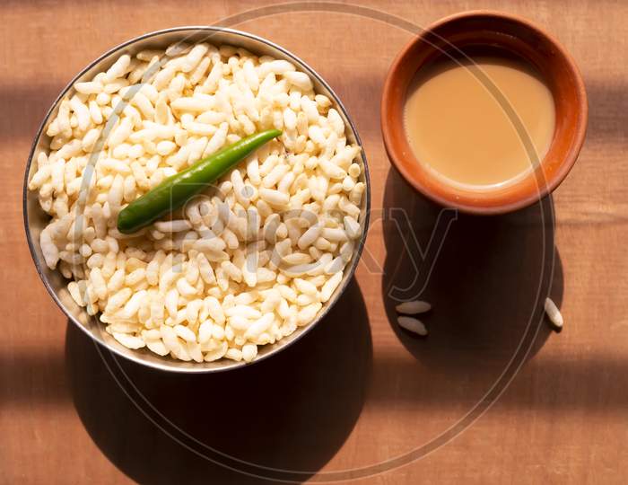 puffed rice and a green chili on a steel bowl with fresh hot tea on a wooden table top