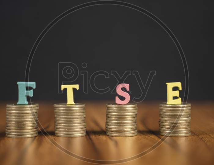 Concept Of Ftse Or Financial Times Stock Exchange Showing With Coins And Letters On Black Background.