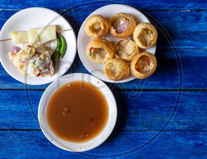 Panipuri Or Golgappa With Tamarind Chutney, Chili And Spicy Potato Stuff In Plates Isolated On Wooden Background, Also Known As Phuchka, Paani Patashi, Gup Chup