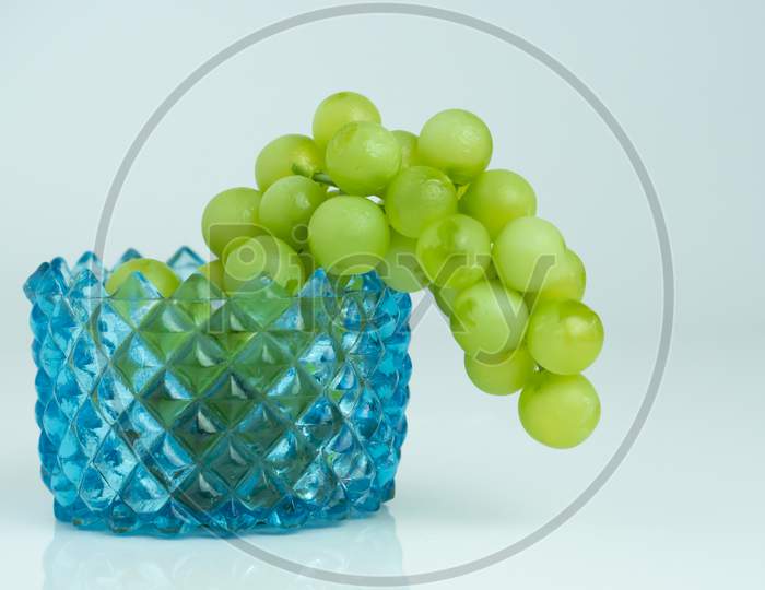 Green grapes on blue glass bowl with white background