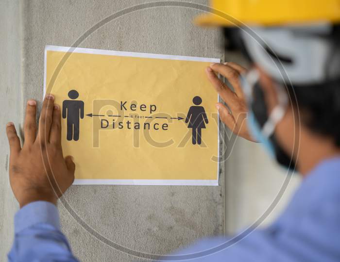 Worker Pasting Keep 6 Feet Distance On Wall At Work Place Or Construction Site Due To Coronavirus Or Covid-19 Pandemic - Concept Of Safety Measures, Back To Work, New Normal And Protection.