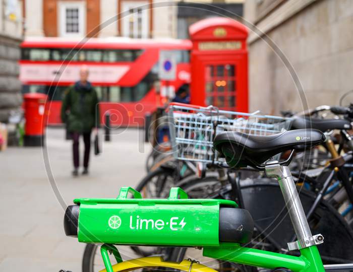 The Rear Mounted Battery Of A Lime Electric Assist Rental Bike With Out Of Focus Traditional Red London Double Decker Bus, Red Phone Box And Red Post Box In The Background