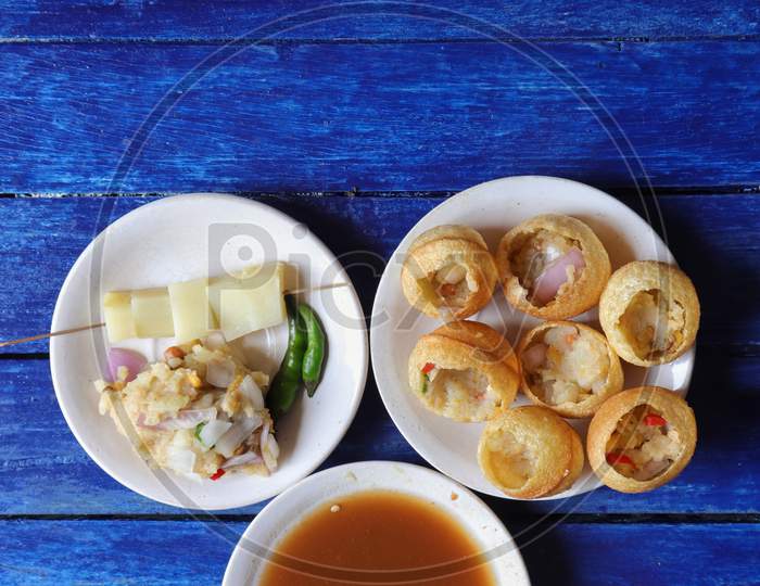 Panipuri Or Golgappa With Tamarind Chutney, Chili And Spicy Potato Stuff In Plates Isolated On Blue Wooden Background In Vertical Orientation With Copy Space, Also Known As Phuchka