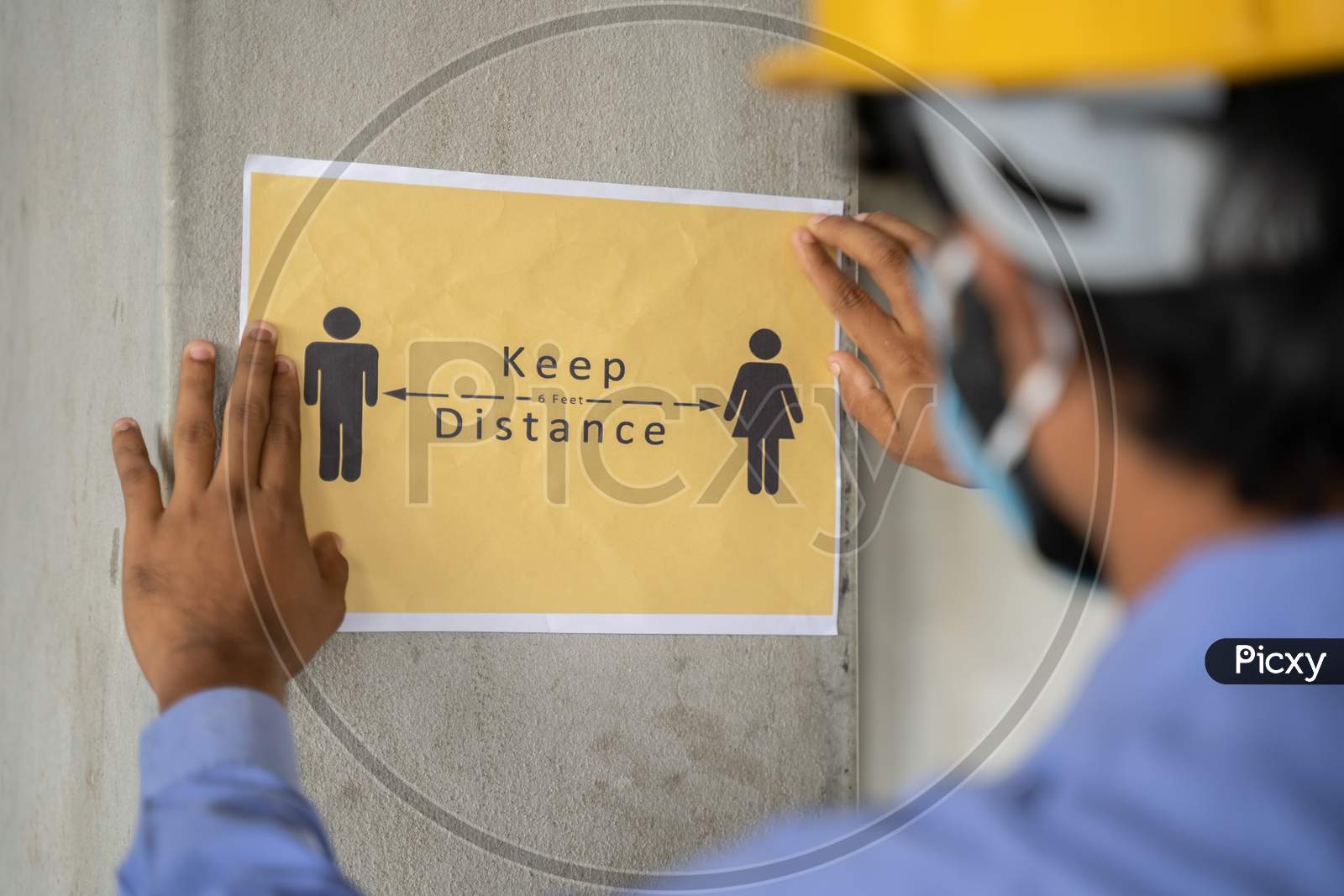 Worker Pasting Keep 6 Feet Distance On Wall At Work Place Or Construction Site Due To Coronavirus Or Covid-19 Pandemic - Concept Of Safety Measures, Back To Work, New Normal And Protection.