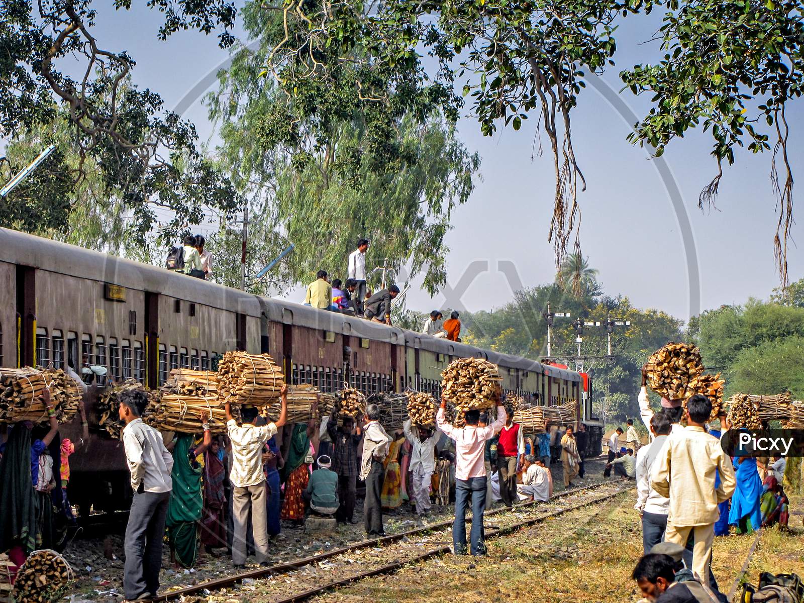Local villagers with wood waiting for their train as pairing train waits for crossing.