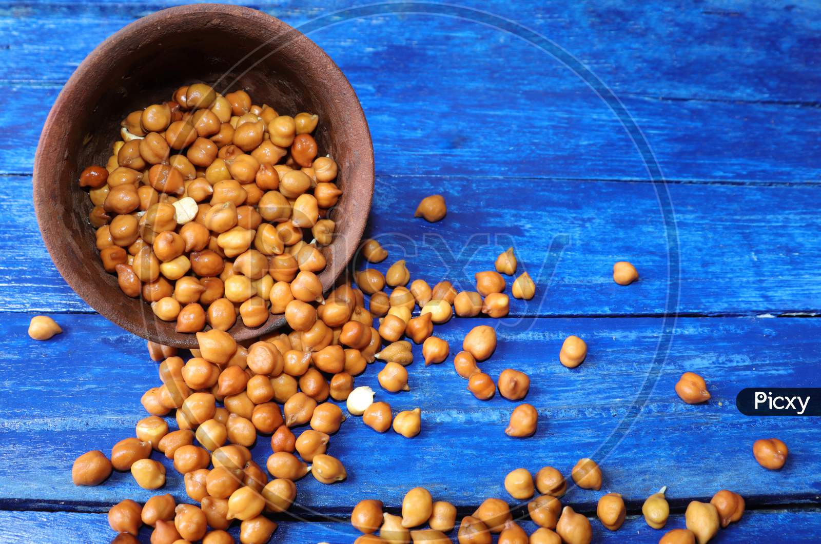Wet Chickpea Or Garbanzo Bean Coming Out Of A Clay Bowl Isolated On Blue Colored Wooden Background With Copy Space