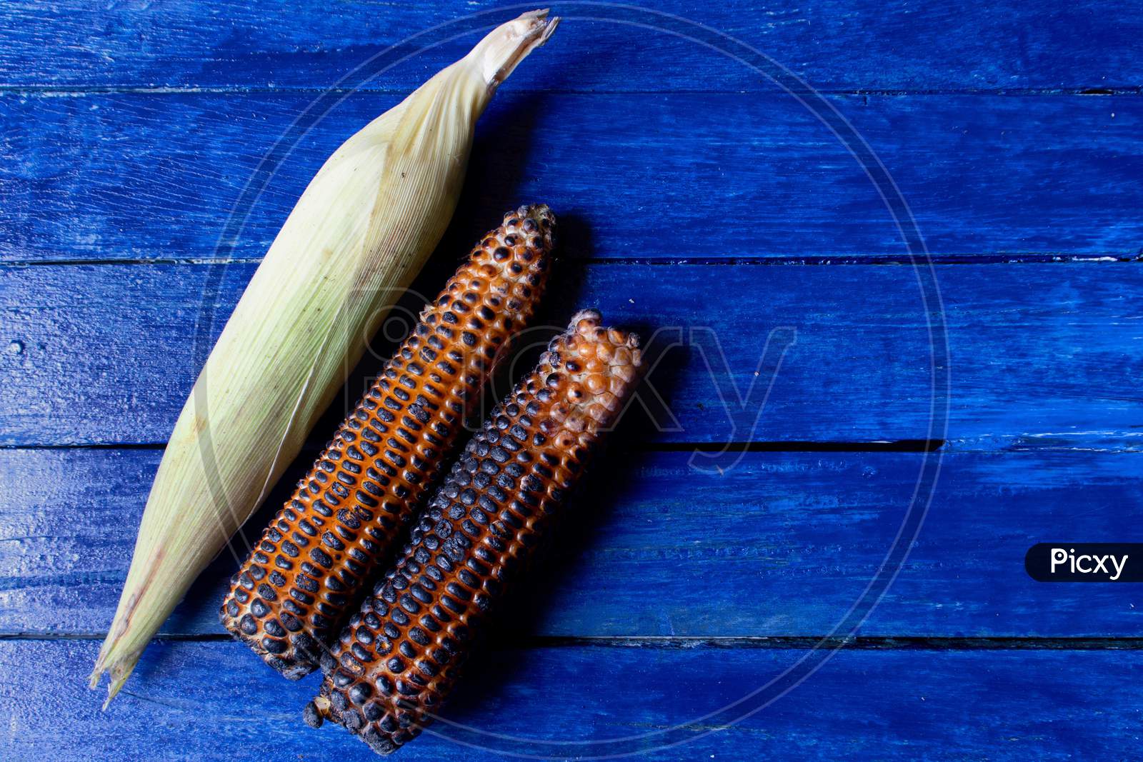 Corns Or Maizes Isolated On Blue Wooden Background With Copy Space