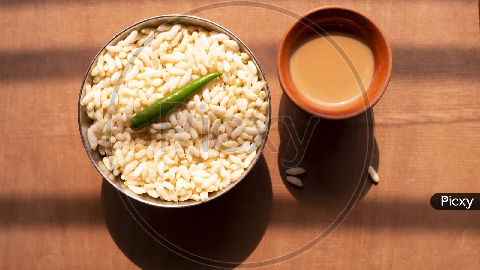 puffed rice and a green chili on a steel bowl with fresh hot tea on a wooden table top