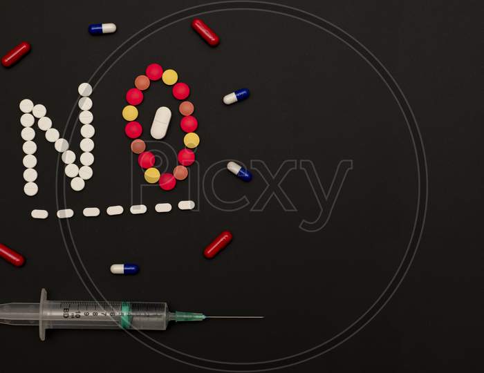 Pills arranged against a dark background forming the word NO.
