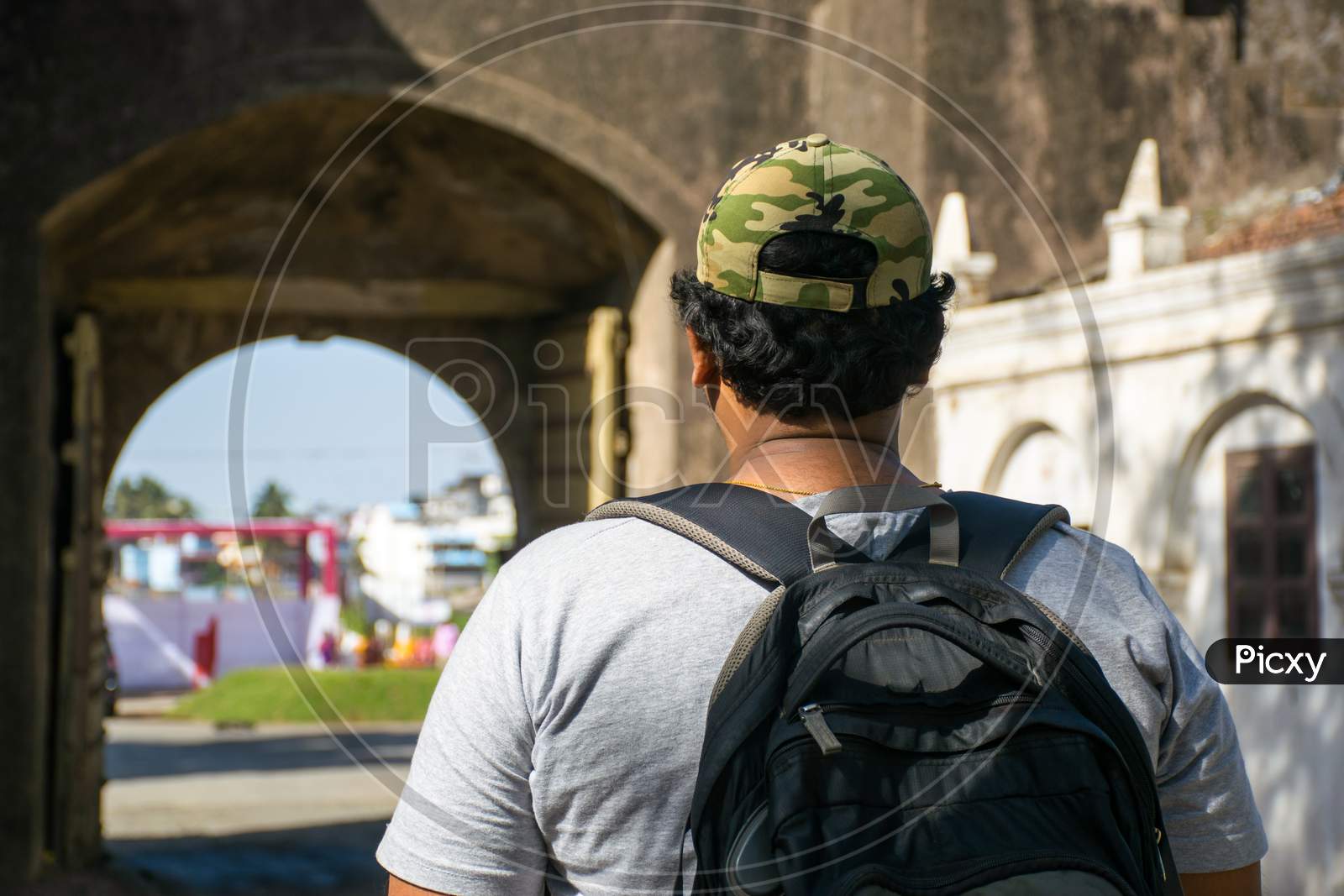 Rear Portrait Of Young Indian Traveler With Backpack And Cap Looking At The Perimeter Wall Of A Fort In India
