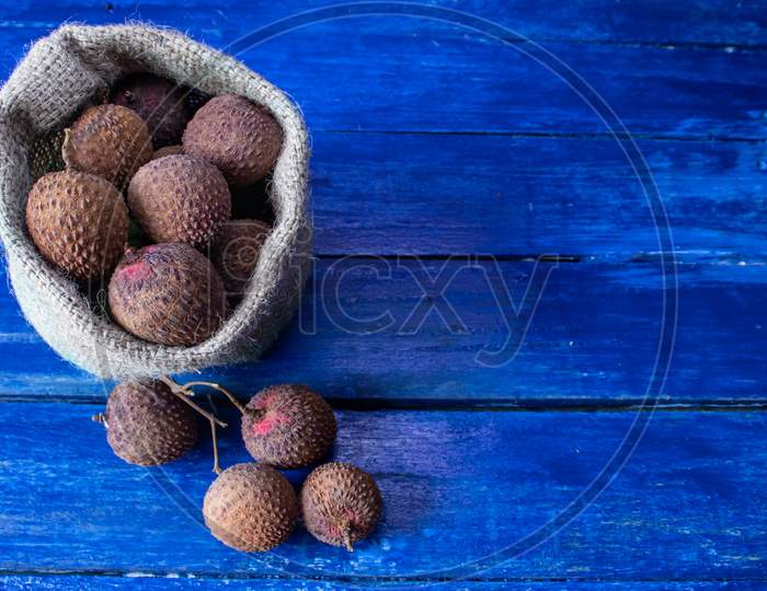 Lychee Or Litchi Fruits In Jute Sack Isolated On Blue Colored Wooden Background With Copy Space