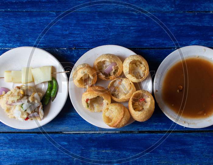 Panipuri Or Golgappa With Tamarind Chutney, Chili And Spicy Potato Stuff In Plates Isolated On Blue Wooden Background In Horizontal Orientation, Also Known As Phuchka