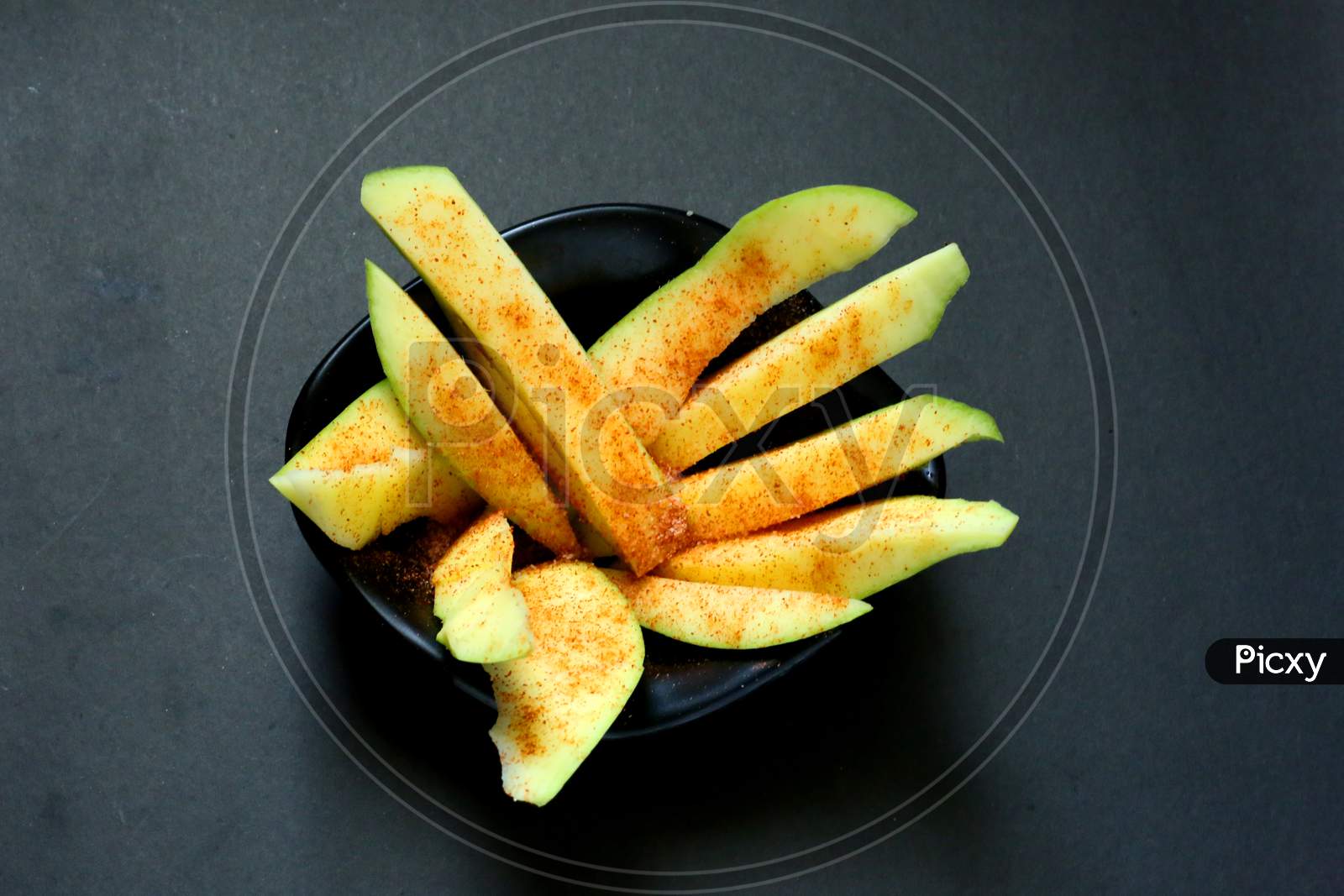 Raw Mango Slices With Salt And Chilli Powder On Isolated Black Background.