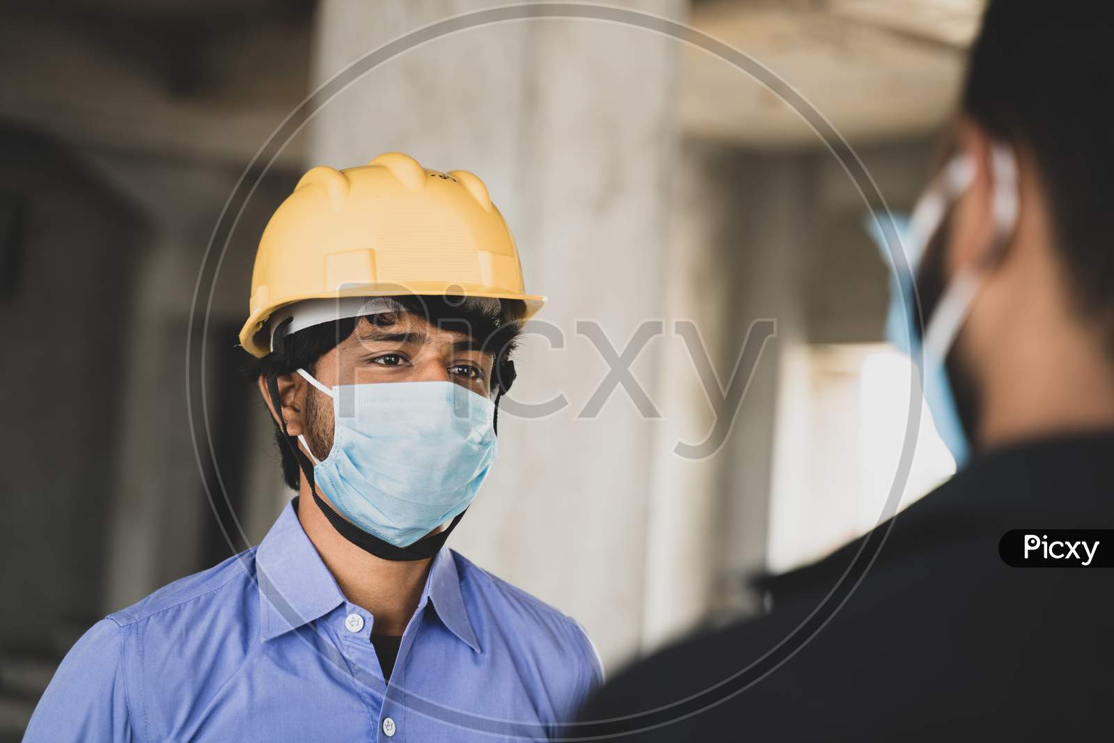 Two Construction Workers Or Engineers At Site Talking By Wearing Medical Face Mask While Maintaining Social Distance - Concept Of Business, Industry Reopen Or Covid-19 Safety Measures At Workplace.