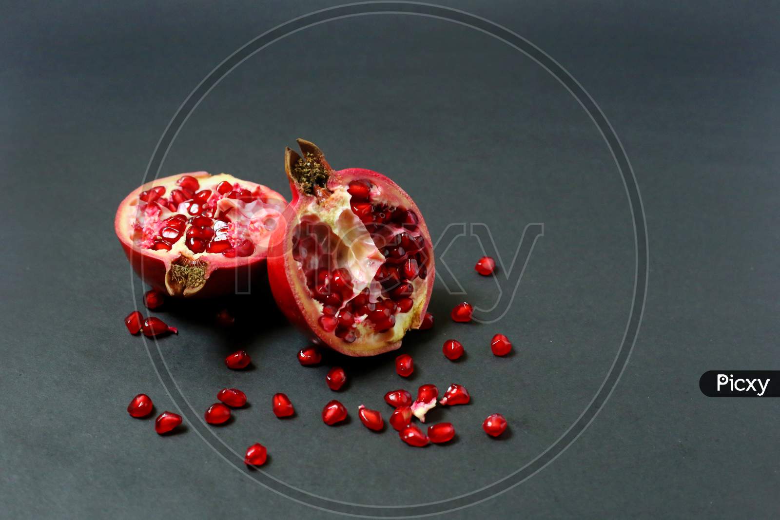 Juicy Pomegranate Fruit Isolated On Dark Background. Ripe Pomegranate Rich Red Color, Ripped In Half With Seeds Around