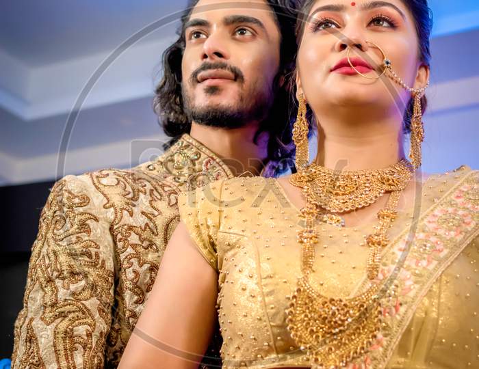 August 2019, Kolkata, India: Indian Groom Dressed In Sherwani With Stunning Bride Standing With Glamorous Outfit And Jewellery With Makeup And Hold Each Hand In A Banquet Hall