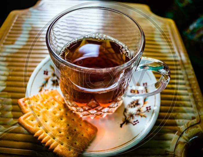 Creative Close-up Photography of A Cup of Hot Tea On The Small Textured Table. Red, black tea in a transparent glass mug served with biscuit on a plate. Herbal Green Tea With Breakfast In The Morning.