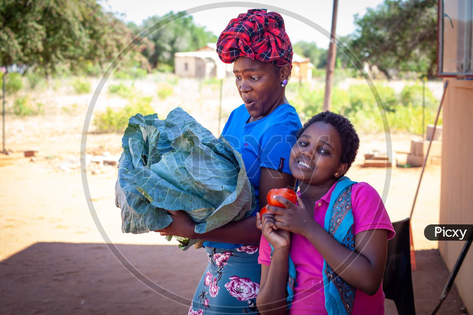 An African Woman With Children Holding A Cabbage And Tomatoes