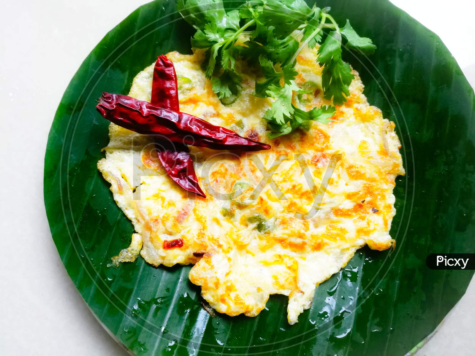 Egg Omelette With Coriander Leaves And Red Chillies In A Banana Leaf.
