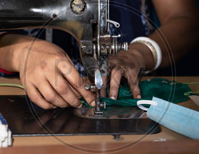 Indian Woman Working On Old Sewing Machine - Making Homemade Face Masks Against Coronavirus Or Covid19 Spreading, Closeup Detail On Moving Needle And Fingers Holding Fabric