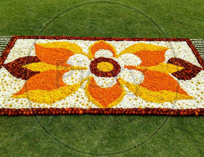 A Colorful Flower Rangoli On A Grass Field. Rangoli Made By Lots Of Yellow, Red And Orange Colored Marigold Flowers, White Chrysanthemum Flowers And Tuberose Flowers.