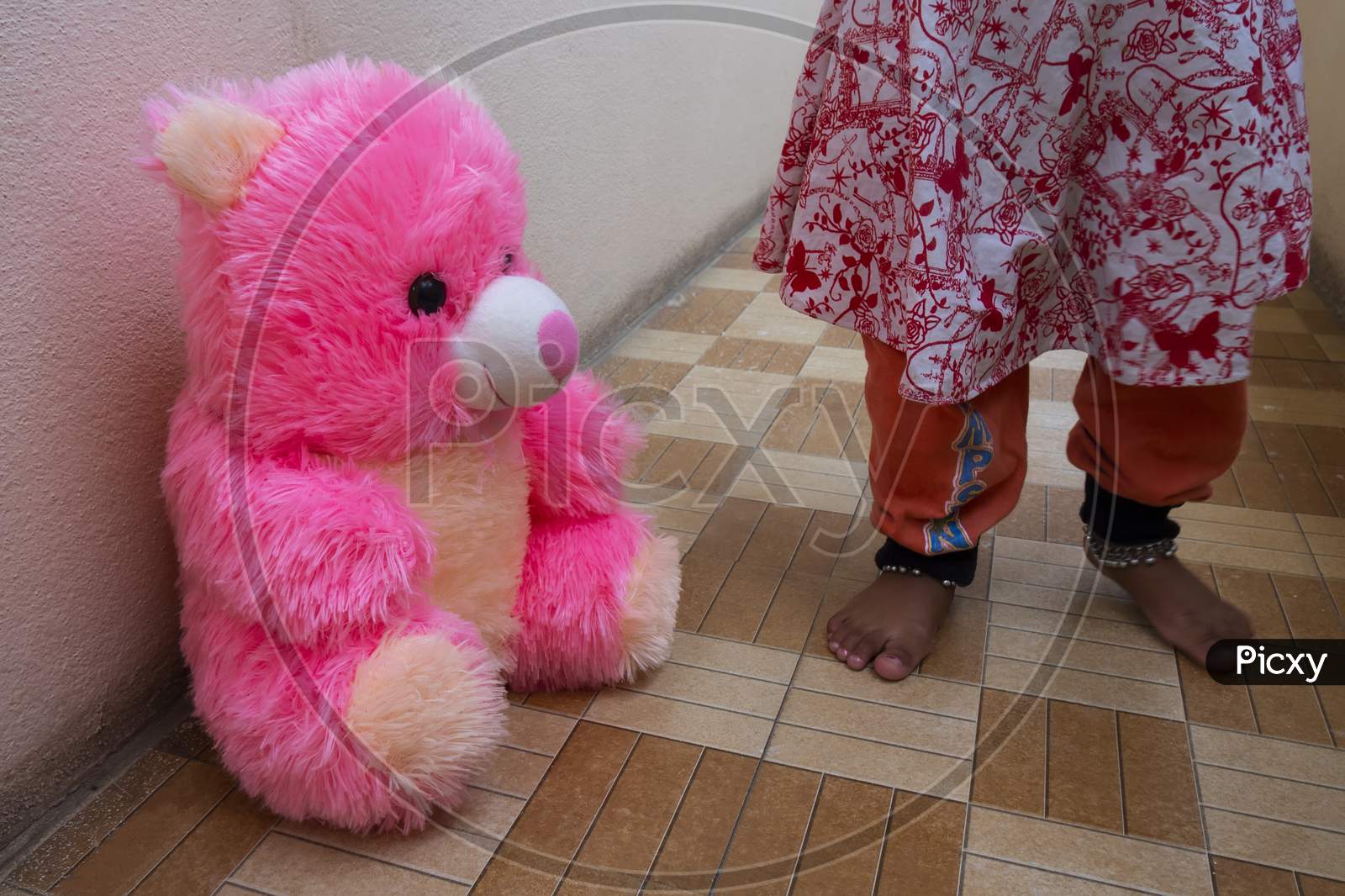 Close Shot Of Pink Teddy Bear Sitting On Floor With Baby Girl Legs Background
