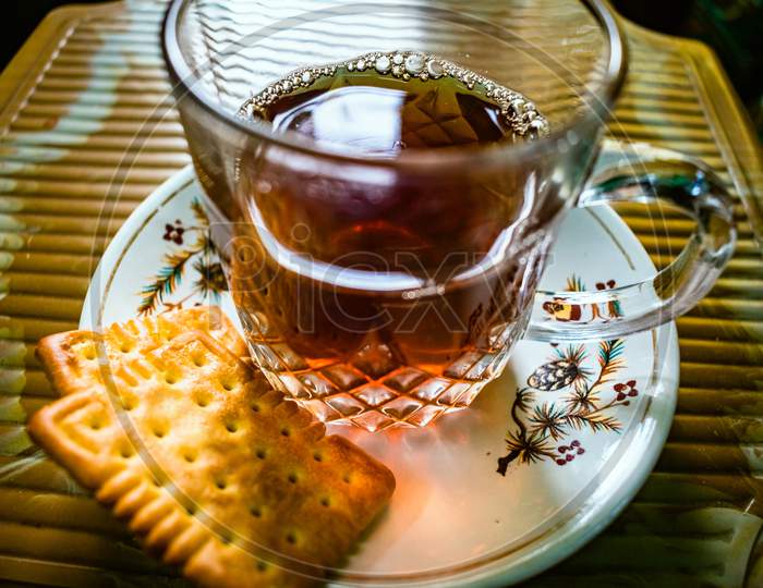 Creative Close-up Photography of A Cup of Hot Tea On The Small Textured Table. Red, black tea in a transparent glass mug served with biscuit on a plate. Herbal Green Tea With Breakfast In The Morning.