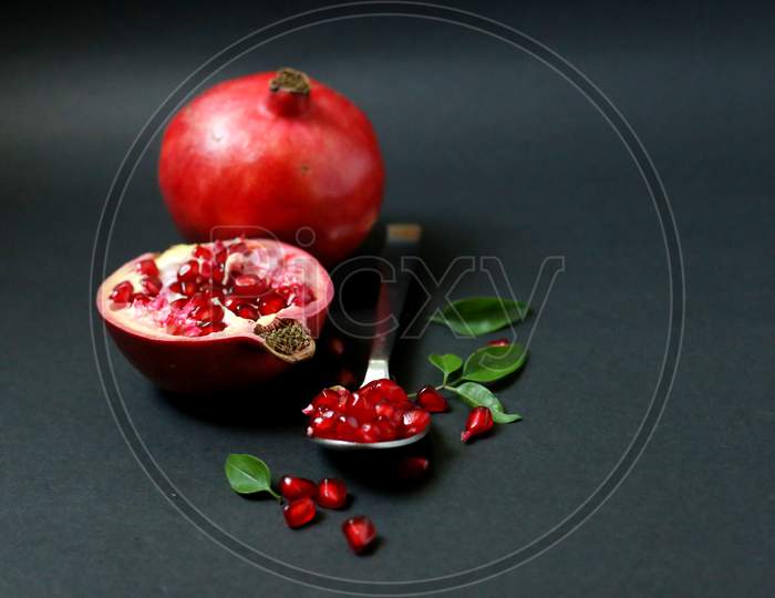 Juicy Pomegranate Fruit Isolated On Dark Background. Red juice pomegranate on dark background. Ripe pomegranate with leaves on a dark background