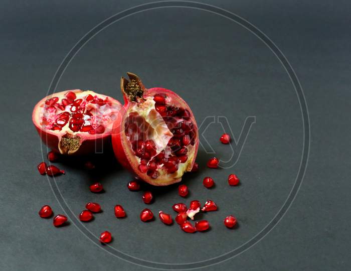 Juicy Pomegranate Fruit Isolated On Dark Background. Ripe Pomegranate Rich Red Color, Ripped In Half With Seeds Around