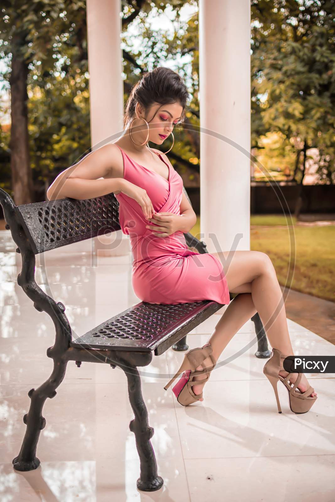Shantiniketan, India. Fashion Portrait Of Beautiful Indian Young Girl Sitting On A Bench, Wearing A Pink Dress, Sunny Day In The Park, Relaxing, After Work Business Woman. September 2019