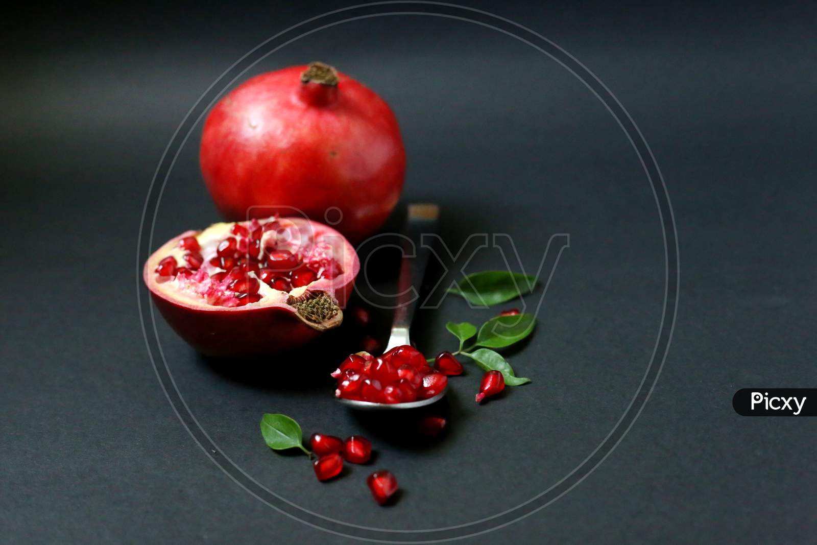 Juicy Pomegranate Fruit Isolated On Dark Background. Red juice pomegranate on dark background. Ripe pomegranate with leaves on a dark background