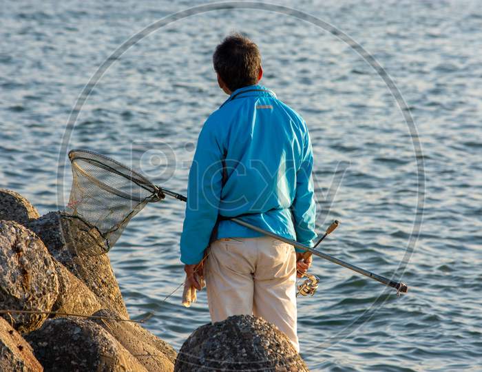 Japanese Man With A Fishing Net Rod Fishing At Seashore In Osaka Bay, Japan