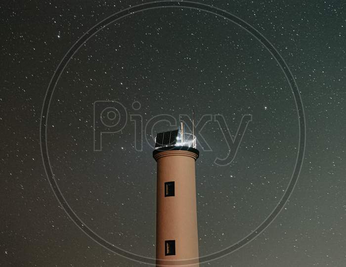 A Close Up Of A White Lighthouse With A Sky Filled Of Stars