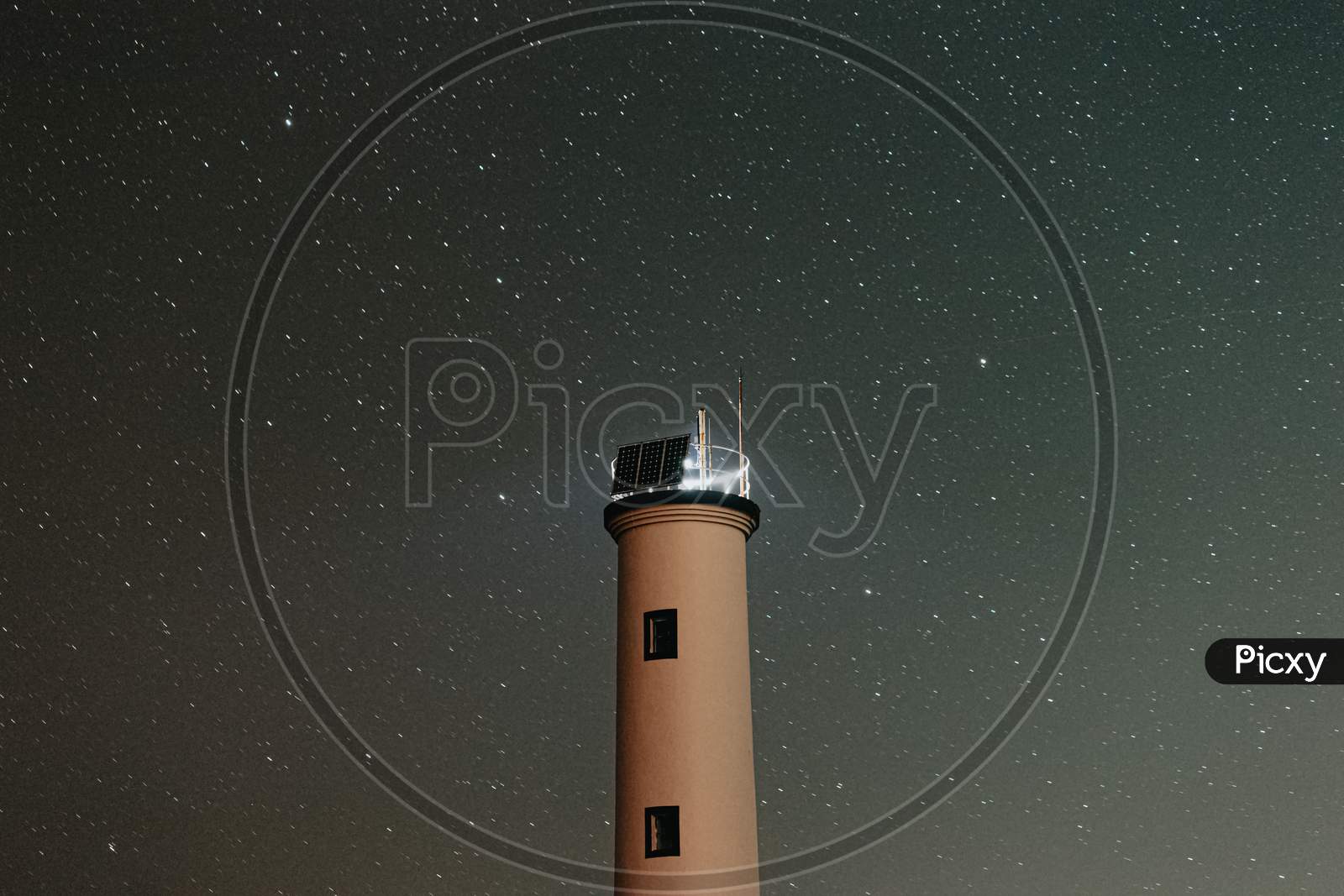 A Close Up Of A White Lighthouse With A Sky Filled Of Stars