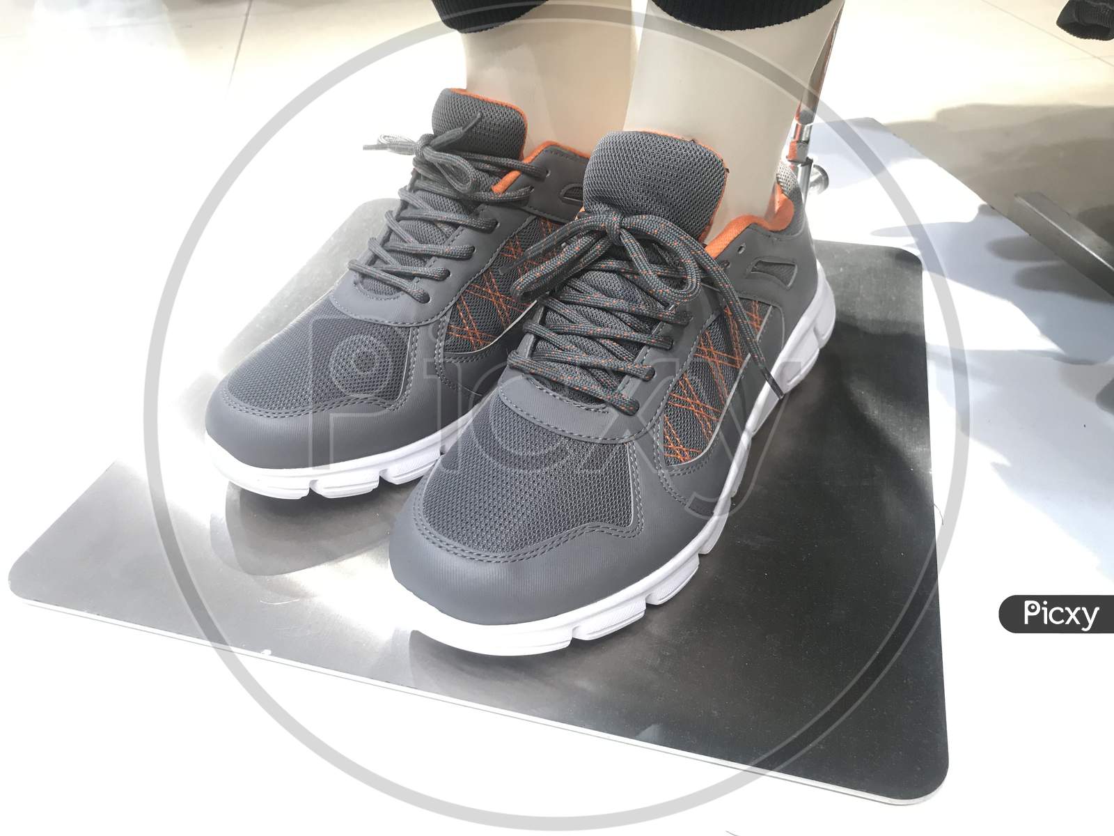 Grey Color Pair Of Sneakers Wore By A Garments Toy For Demo On A Stainless Steel And Fixed Rigid For Marketing Of Sports Shoes For Athletes