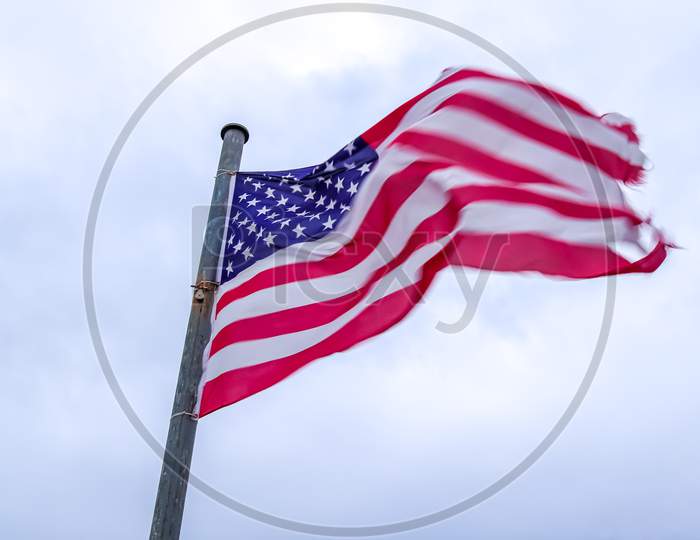 Usa Flag At A Flagpole Moving Slowly In The Wind Against The Sky