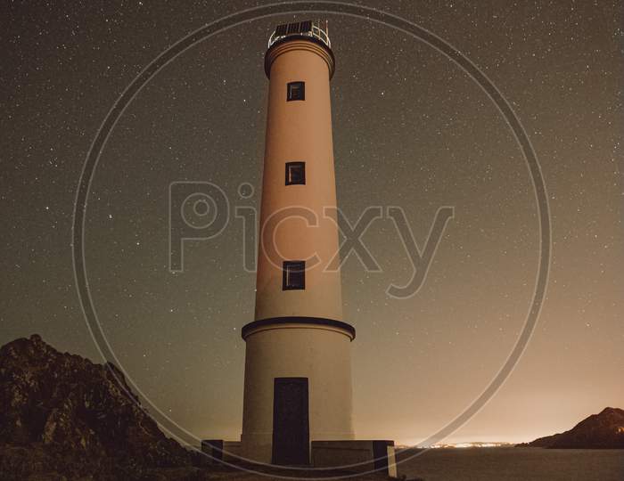 A White Lighthouse With A Sky Filled With Stars As A Background