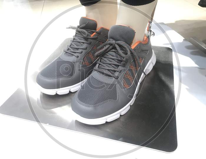 Grey Color Pair Of Sneakers Wore By A Garments Toy For Demo On A Stainless Steel And Fixed Rigid For Marketing Of Sports Shoes For Athletes