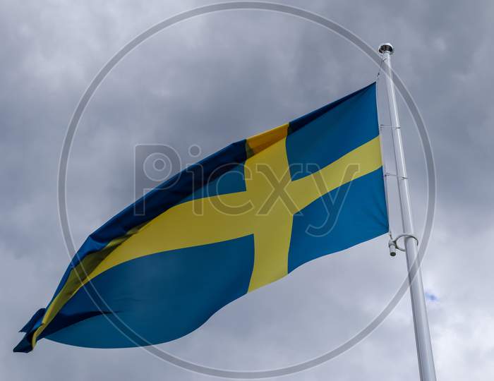Sweden Flag At A Flagpole Moving Slowly In The Wind Against The Sky