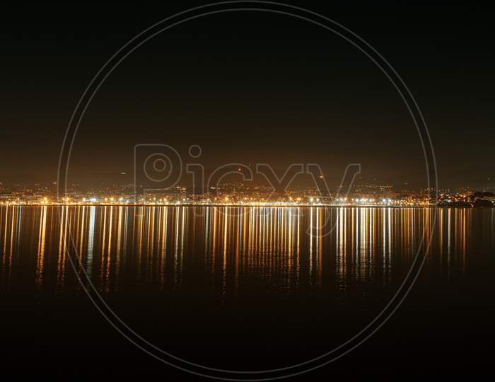 A Panoramic View Of The City Lights Reflecting In The Sea During The Night