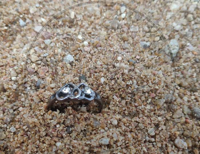 Wedding rings on the sand with rocks in a shape of a heart
