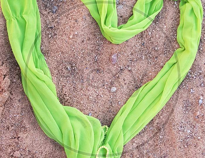 Green dupatta heart shape on sand background