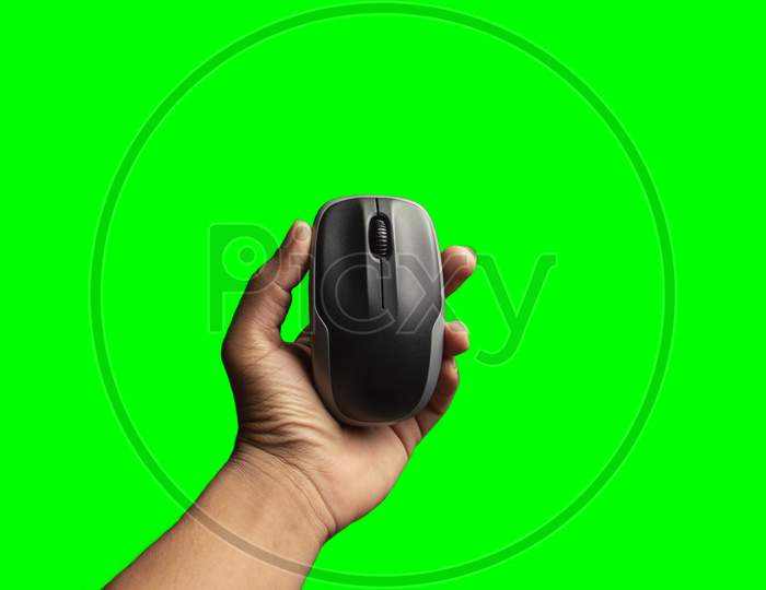 Hand Holding Computer Mouse Isolated On The Green Background. Above View Of Computer Mouse On Green Background. Black And Grey Computer Mouse.