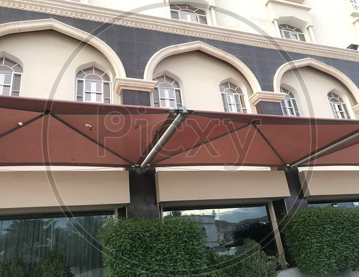 Brown Color Fabric Tensile Shade Structure In Front Of An Hotel Building For Shaded Area