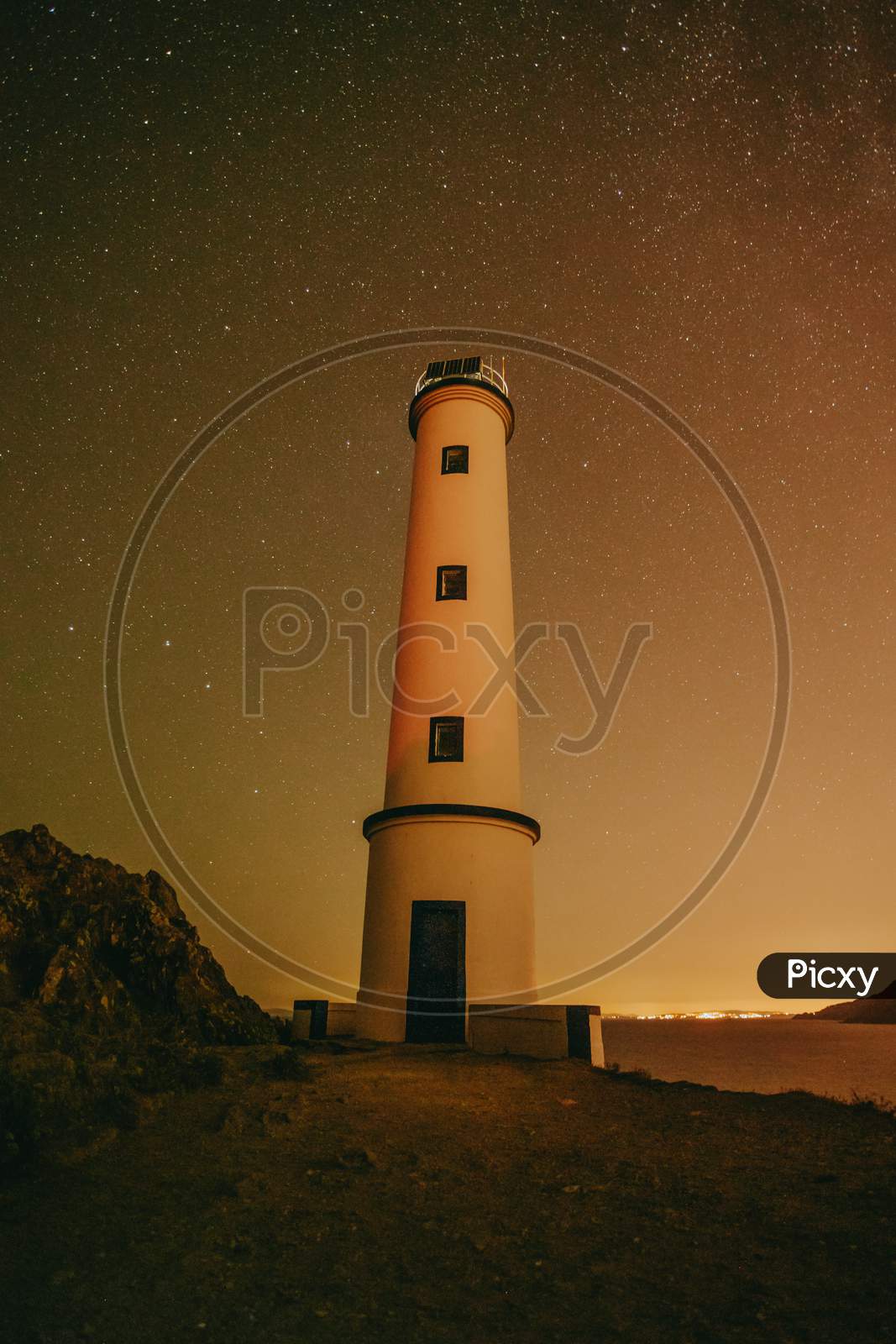 A White Lighthouse With A Sky Filled With Stars As A Background