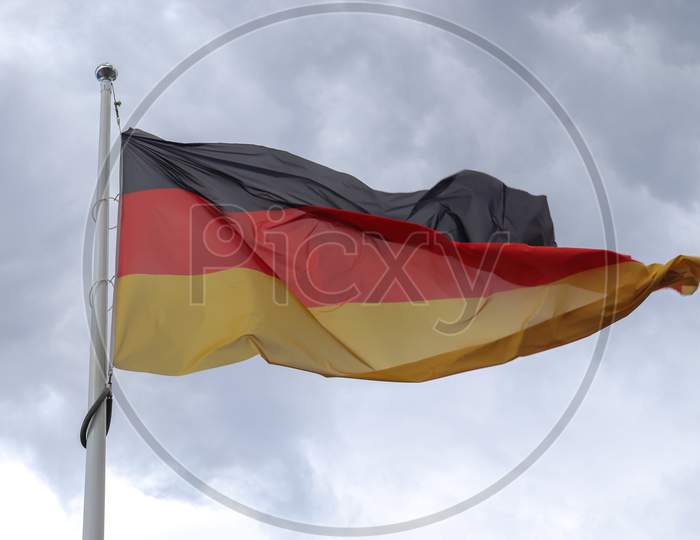 Germany Flag At A Flagpole Moving Slowly In The Wind Against The Sky