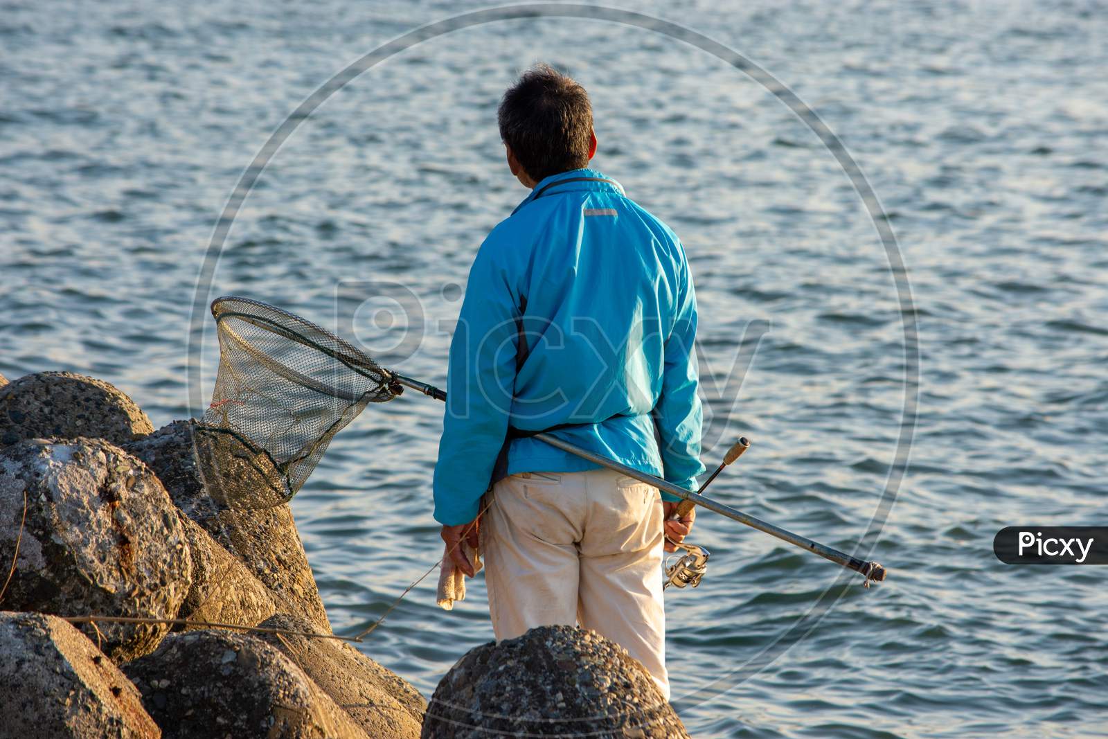 Japanese Man With A Fishing Net Rod Fishing At Seashore In Osaka Bay, Japan