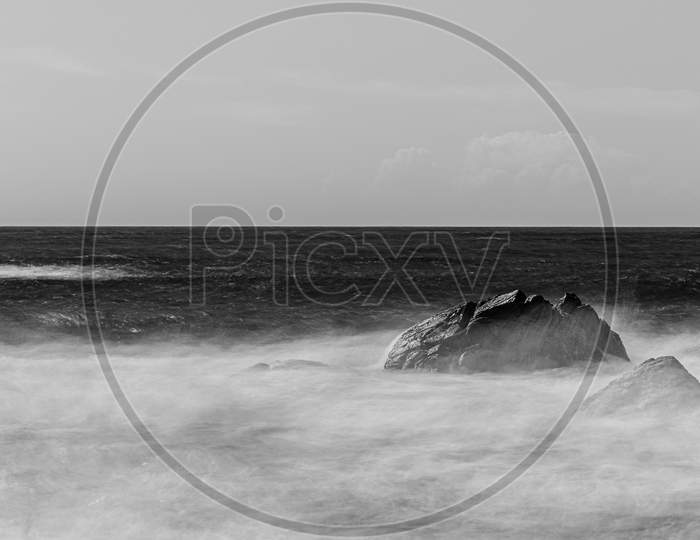 Long Exposure Black And White Shot Of A Rock In The Middle Of The Wild Sea With A Bright Horizon
